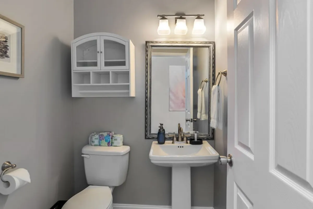 A well-appointed bathroom featuring a sink with a mirror, stylish light fixtures, a toilet, and a shelf with toiletries. The space is organized and serene, perfectly suited for personal grooming and relaxation.