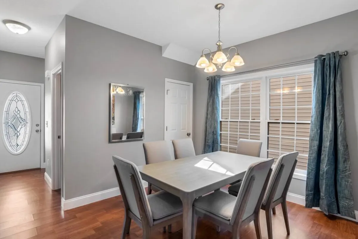 A dining area with a welcoming table set beneath a chandelier, flanked by a window and a decorative mirror. The layout encourages gatherings, family dinners, or casual conversations, fitting the theme of shared spaces.