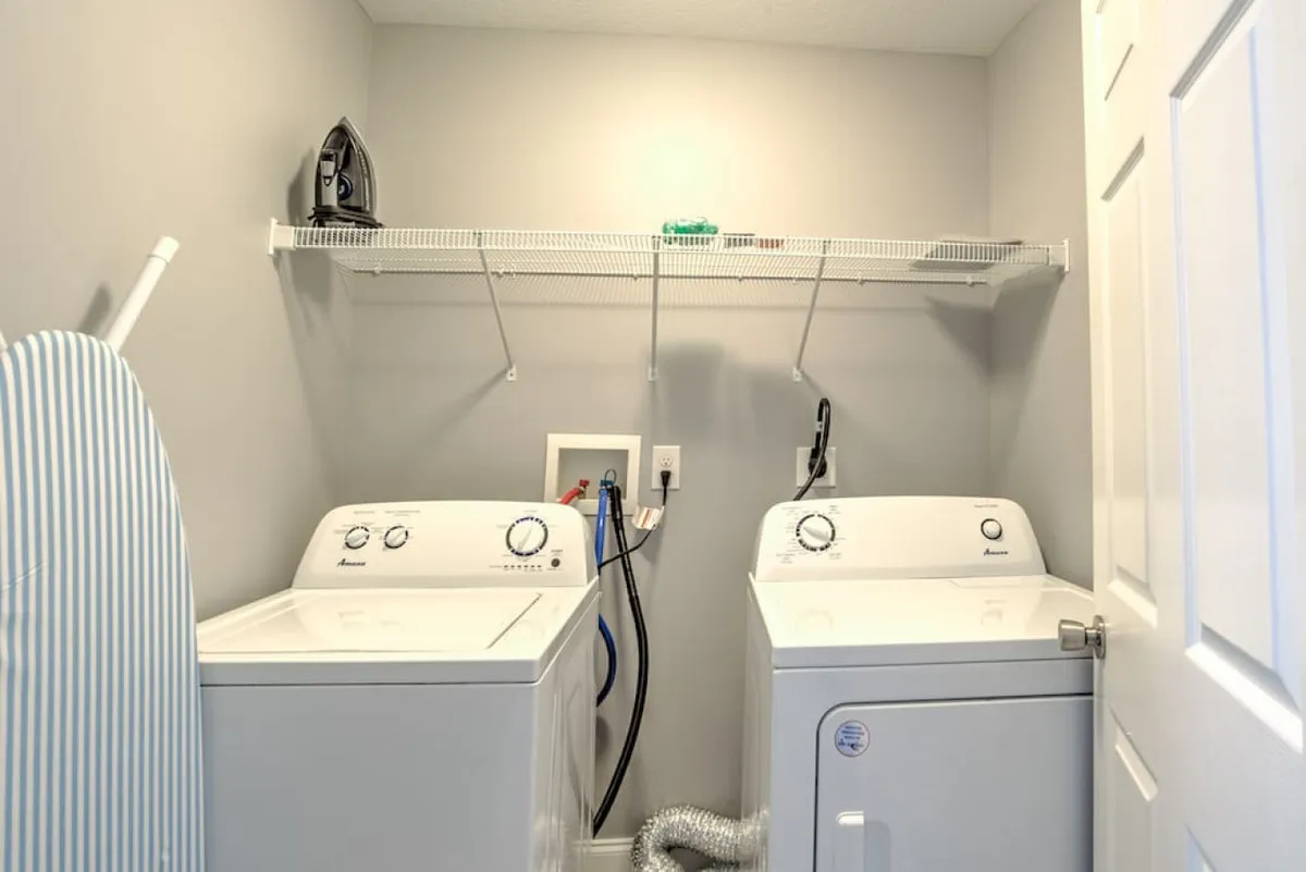This image captures the laundry area with a washing machine, dryer, ironing board, and iron. The space is organized and practical, emphasizing utility and convenience for guests managing outdoor gear or daily needs.
