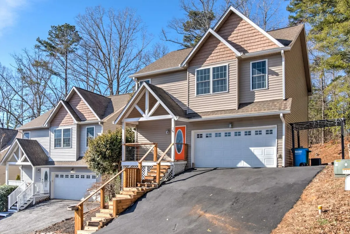This image showcases the home's exterior, highlighting the front porch, decorative entry door, landscaped yard, and driveway. The driveway is visible, suggesting ample parking and ease of access to the home. The overall scene is bright and welcoming, with natural elements and inviting design cues.