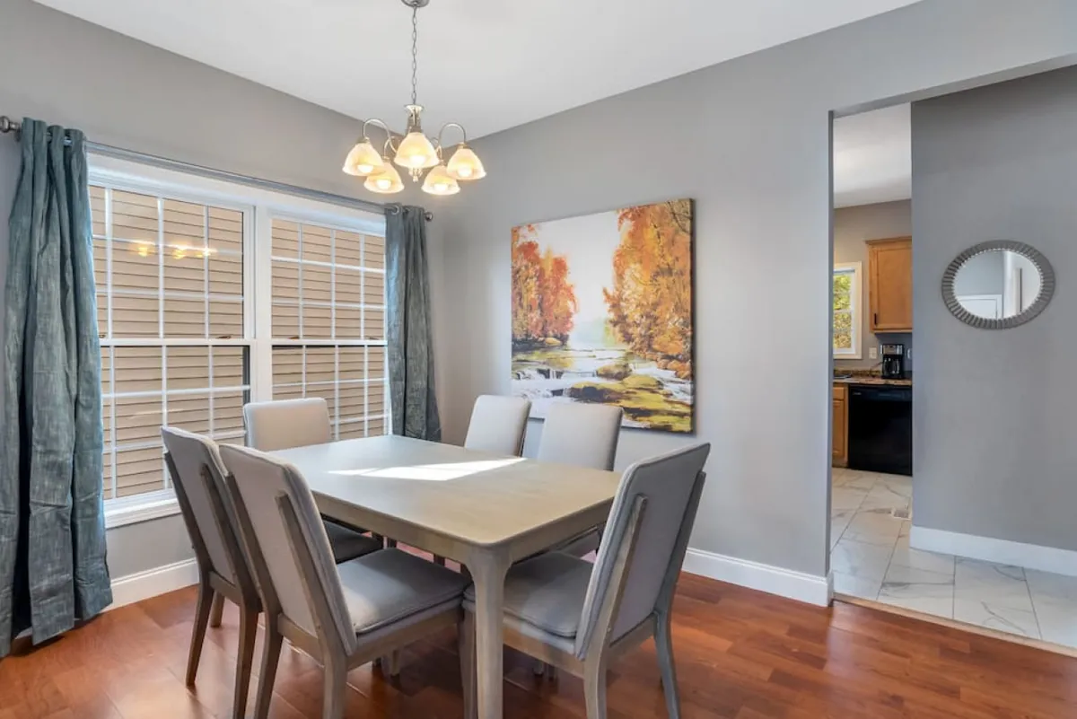 An inviting dining area with a central table set beneath an elegant chandelier, accented by wall artwork and light-diffusing curtains. The space is designed for family dinners, celebrations, and togetherness.