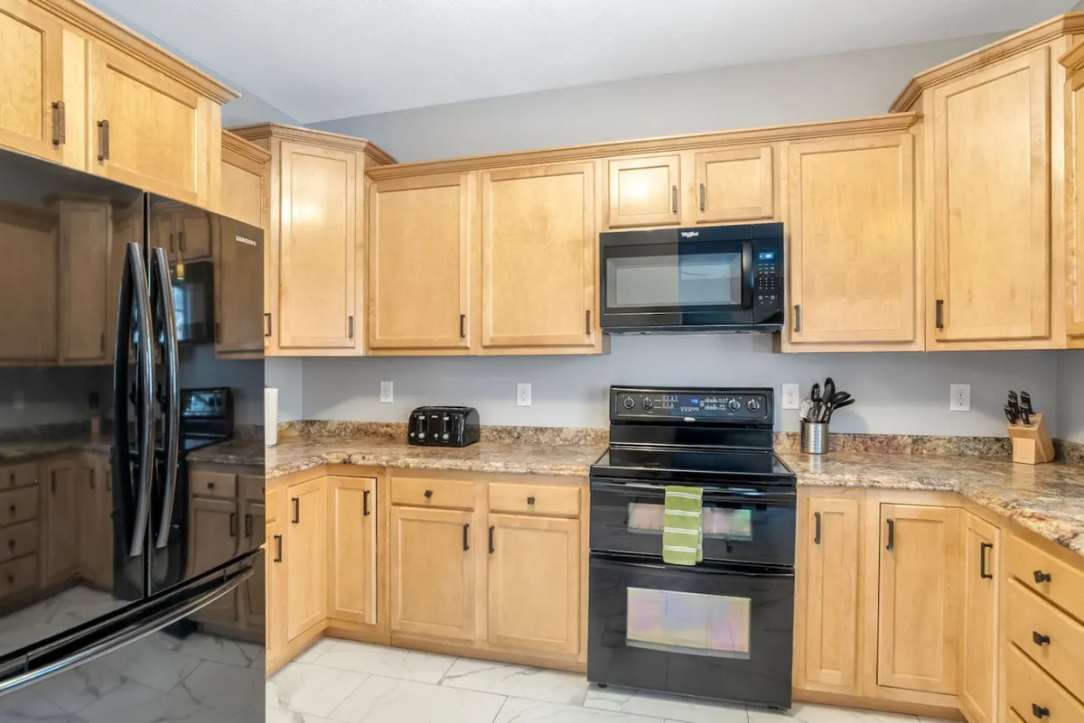 A bright, functional kitchen featuring a black refrigerator and stove, granite countertops, and warm maple cabinetry. The scene is arranged for preparing meals and gathering, exuding an inviting and practical atmosphere ideal for cooking and entertaining.